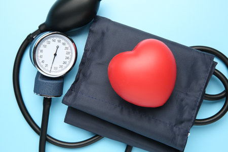 Blood pressure measuring device and heart on light blue background, top view
