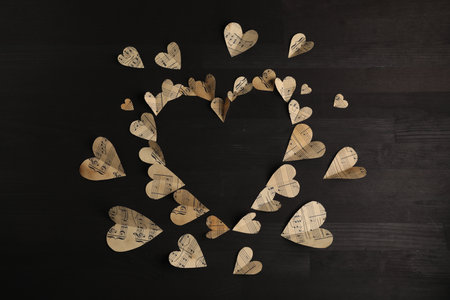 Heart shaped frame made of paper hearts with notes on black wooden table, top view. Space for text