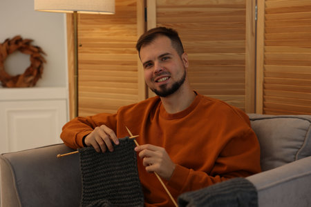 Man knitting with needles in armchair at homeの写真素材