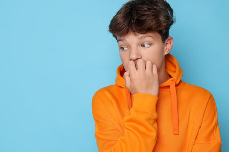 Scared teenage boy on light blue background.の写真素材