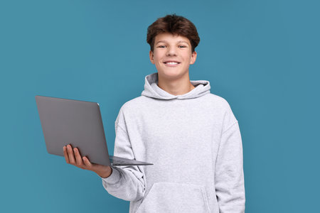 Teenage boy with laptop on light blue background