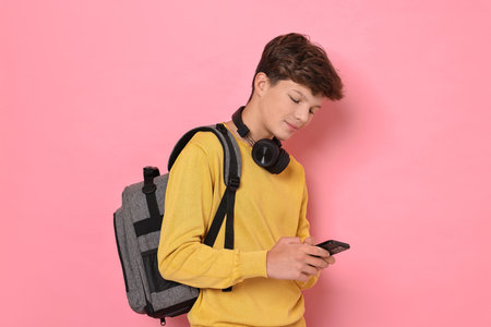 Teenage boy with headphones, smartphone and backpack on pink background