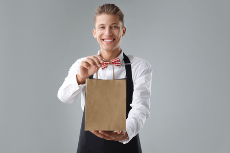 Fast-food worker with paper bag on gray backgroundの写真素材