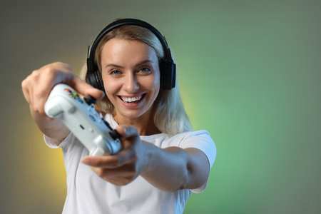 Happy woman in headphones playing video games with controller on color background, space for text