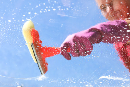 Woman washing window with squeegee tool against blue sky, closeupの写真素材