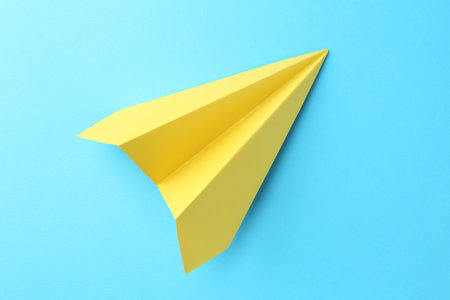 One handmade yellow paper plane on light blue background, top viewの写真素材