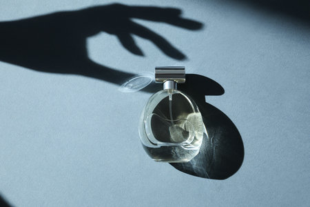 Perfume bottle and shadow of woman's hand on gray background, top view