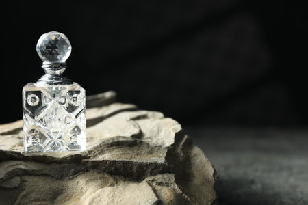 Bottle of fragrant perfume and rock on gray table, space for text