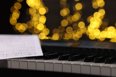 Sheet with musical notes on piano against blurred lights, closeup. Bokeh effectの写真素材