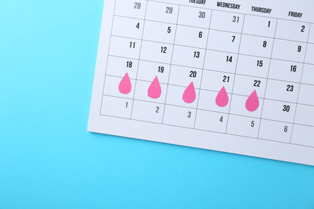 Menstruation. Calendar with marked dates on light blue background, top view