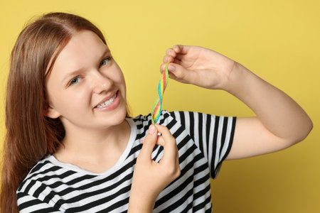 Happy teenage girl with tasty rainbow sour belt on yellow backgroundの写真素材
