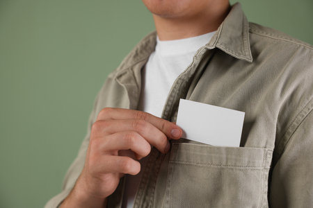 Person taking blank card from pocket of their jacket on green background, closeup. Mockup for design