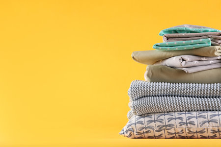 Stack of clean bed linen and pillow on yellow background. Space for text