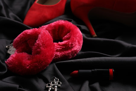 Red fluffy handcuffs, keys, lipstick and shoes on black fabric, closeupの写真素材