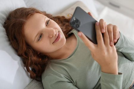 Beautiful teenage girl using smartphone on bed at homeの写真素材