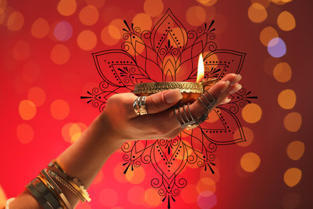 Diwali celebration. Woman holding lit diya lamp on red background with blurred lights, closeupの写真素材