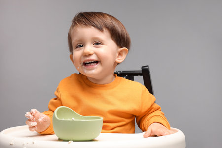Cute little kid eating healthy baby food from bowl in high chair on light gray backgroundの写真素材