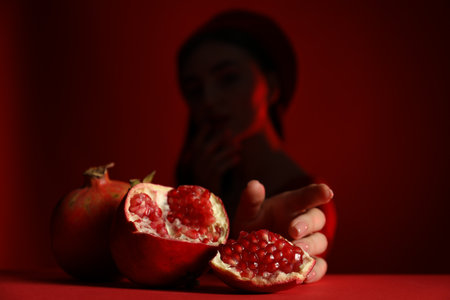 Woman posing against dark red background, focus on ripe pomegranateの写真素材