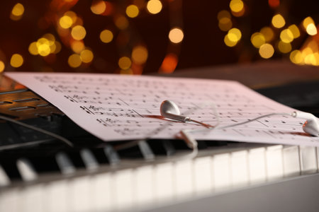 Sheet with musical notes and earphones on piano against blurred lights, closeup. Bokeh effectの写真素材