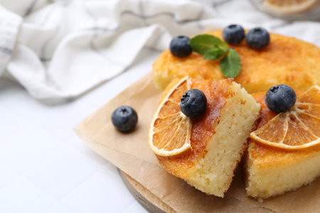 Pieces of delicious semolina cake with blueberries and orange slices on white tiled table, closeup. Space for textの写真素材