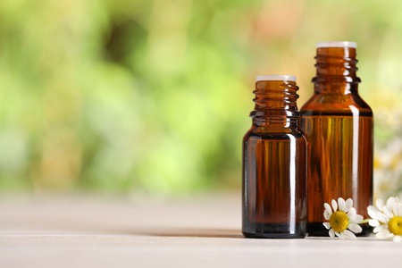 Bottles of essential oil and chamomile flowers on white wooden table against blurred background, closeup. Space for textの写真素材
