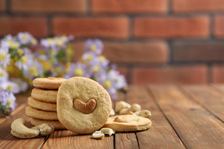 Tasty cashew cookies on wooden table against brick wall, closeup. Space for textの写真素材