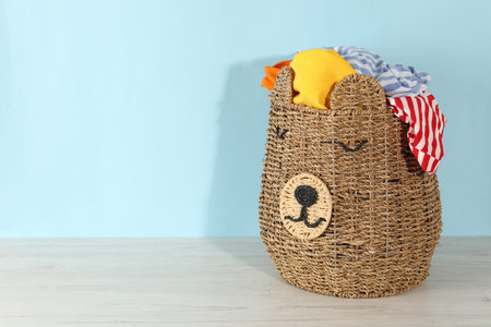 Wicker basket full of laundry on wooden table against light blue background, space for textの写真素材