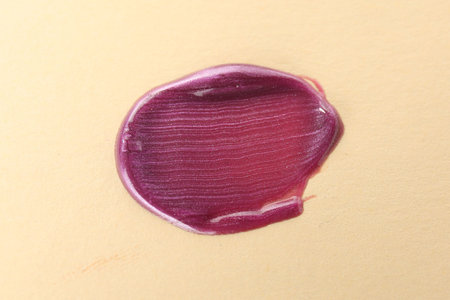 Sample of purple lipgloss on beige background, top view