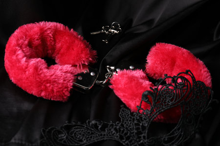 Red fluffy handcuffs, keys and lace mask on black fabric, closeupの写真素材