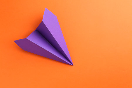 One handmade violet paper plane on orange background, top view. Space for textの写真素材