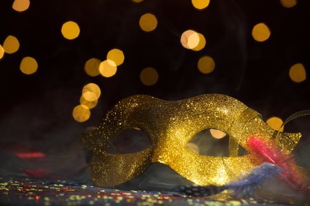 Beautiful carnival mask and confetti in smoke on dark background with blurred lights, closeupの写真素材