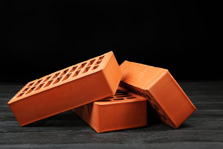 Many red bricks on dark wooden table. Building material