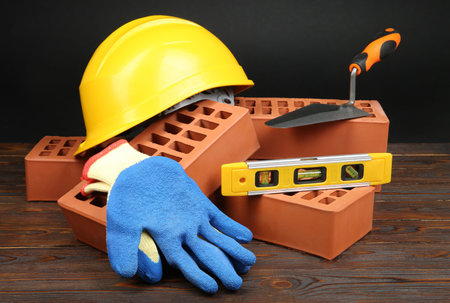 Red bricks, different construction tools and safety equipment on wooden table