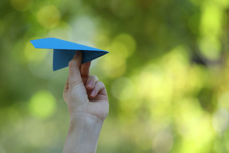 Woman with handmade paper plane on blurred green background, closeup. Space for textの写真素材