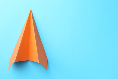 One handmade orange paper plane on light blue background, top view. Space for text