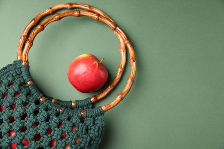 Macrame shopping bag with wooden handles and apple on green background, flat lay. Space for textの写真素材