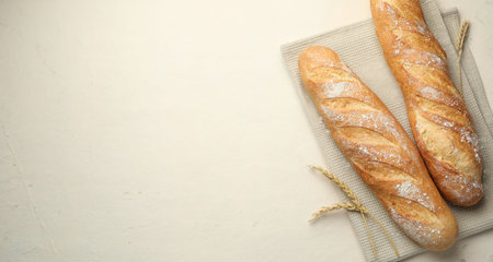 Fresh baguettes and spikes on beige table, flat lay. Space for textの写真素材