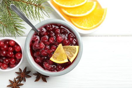 Tasty cranberry sauce, berries, orange, anise and fir branches on white wooden table, flat lay. Space for textの写真素材