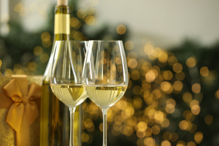 Glasses and bottle of white wine against blurred Christmas lights, closeup. Bokeh effectの写真素材