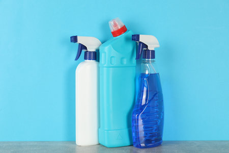 Different cleaning products on gray table against light blue background