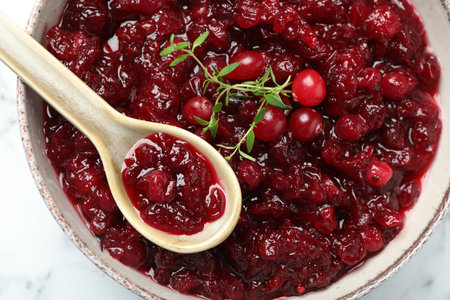 Tasty cranberry sauce in bowl, berries, thyme and spoon on table, top viewの写真素材