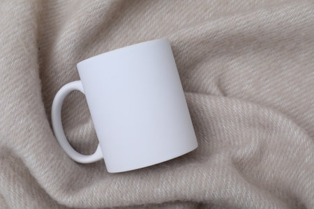 Blank white ceramic mug on beige fabric, top view. Mockup for designの写真素材
