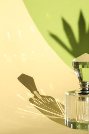 Beautiful perfume bottle on color background against shadow in shape of leafの写真素材