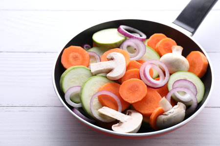 Frying pan with mix of fresh vegetables and mushrooms on white wooden table, closeupの写真素材