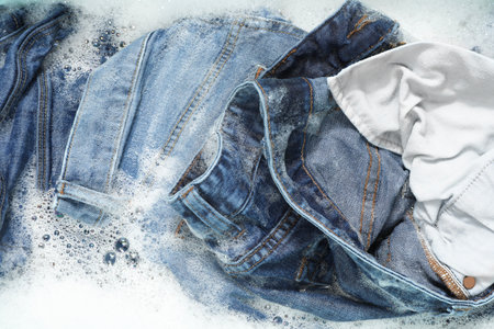 Many different denim clothes in basin with water and soap, top viewの写真素材