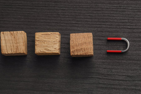 Magnet attracting cubes on black wooden table, flat lay