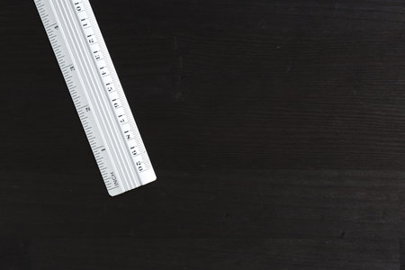 One metal ruler on black wooden table, top view. Space for text