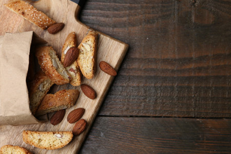 Paper bag with tasty almond biscuits (Cantuccini) and nuts on wooden table, top view. Space for text