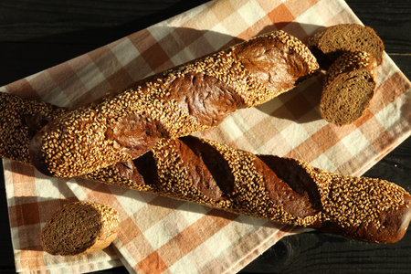 Fresh baguettes with sesame on black wooden table, flat lay