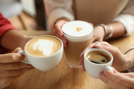 Women with cups of delicious coffee drinks at wooden table in cafe, closeupの写真素材
